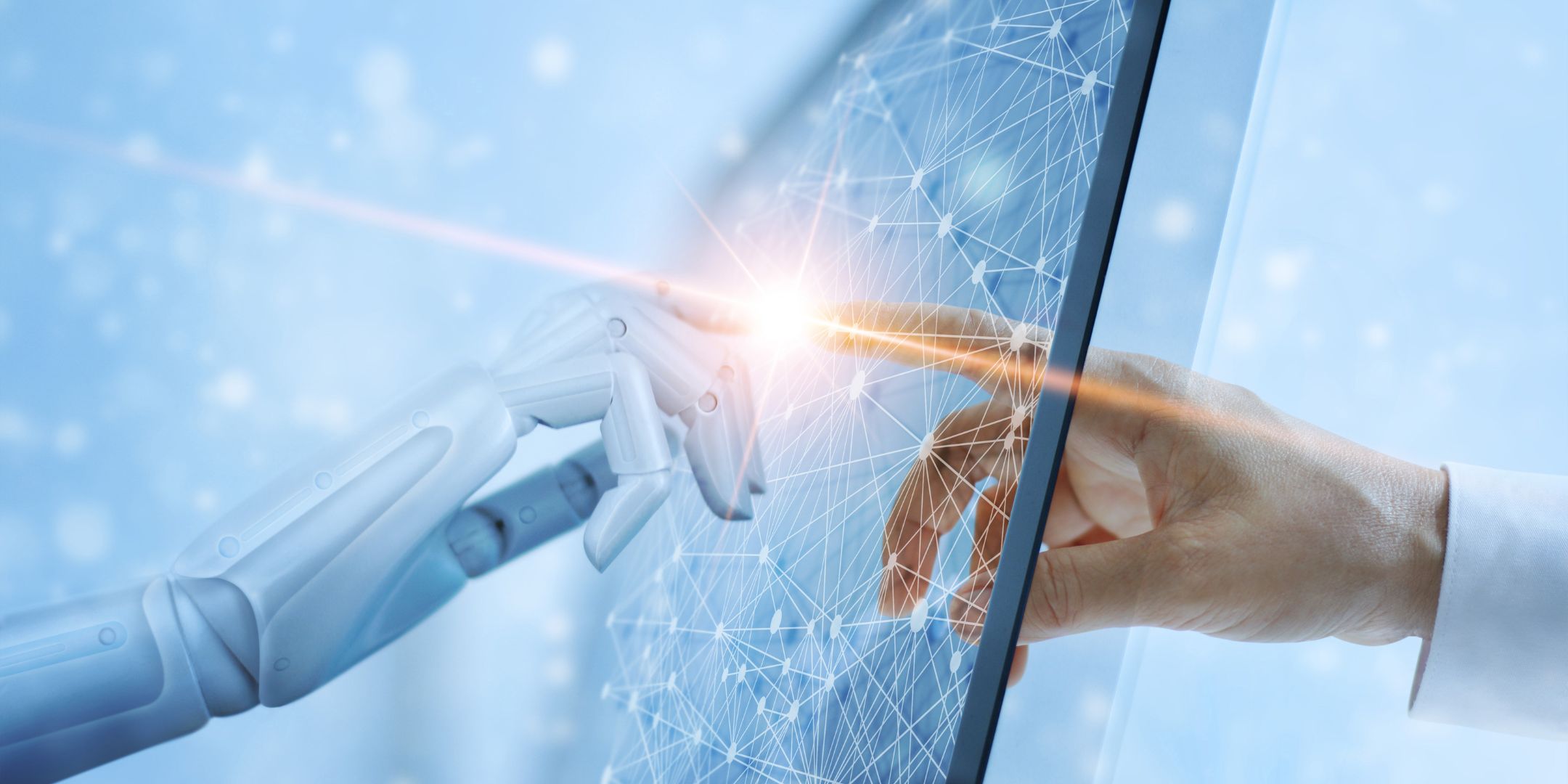 A robotic hand and a human hand touch fingertips through a digital touchscreen interface, symbolizing the connection between artificial intelligence and human intelligence. The screen displays a network of interconnected nodes and lines, representing data or digital communication, with a bright light at the point of contact. The background is softly blurred in blue tones.